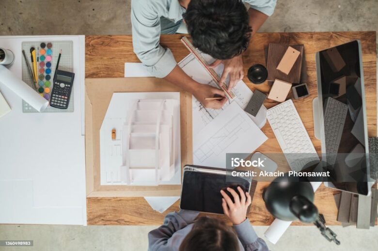 Top view, Team architect design building model with blueprint engaged working together on the desk in office. Architect or engineer working teamwork concept. Selective focus.